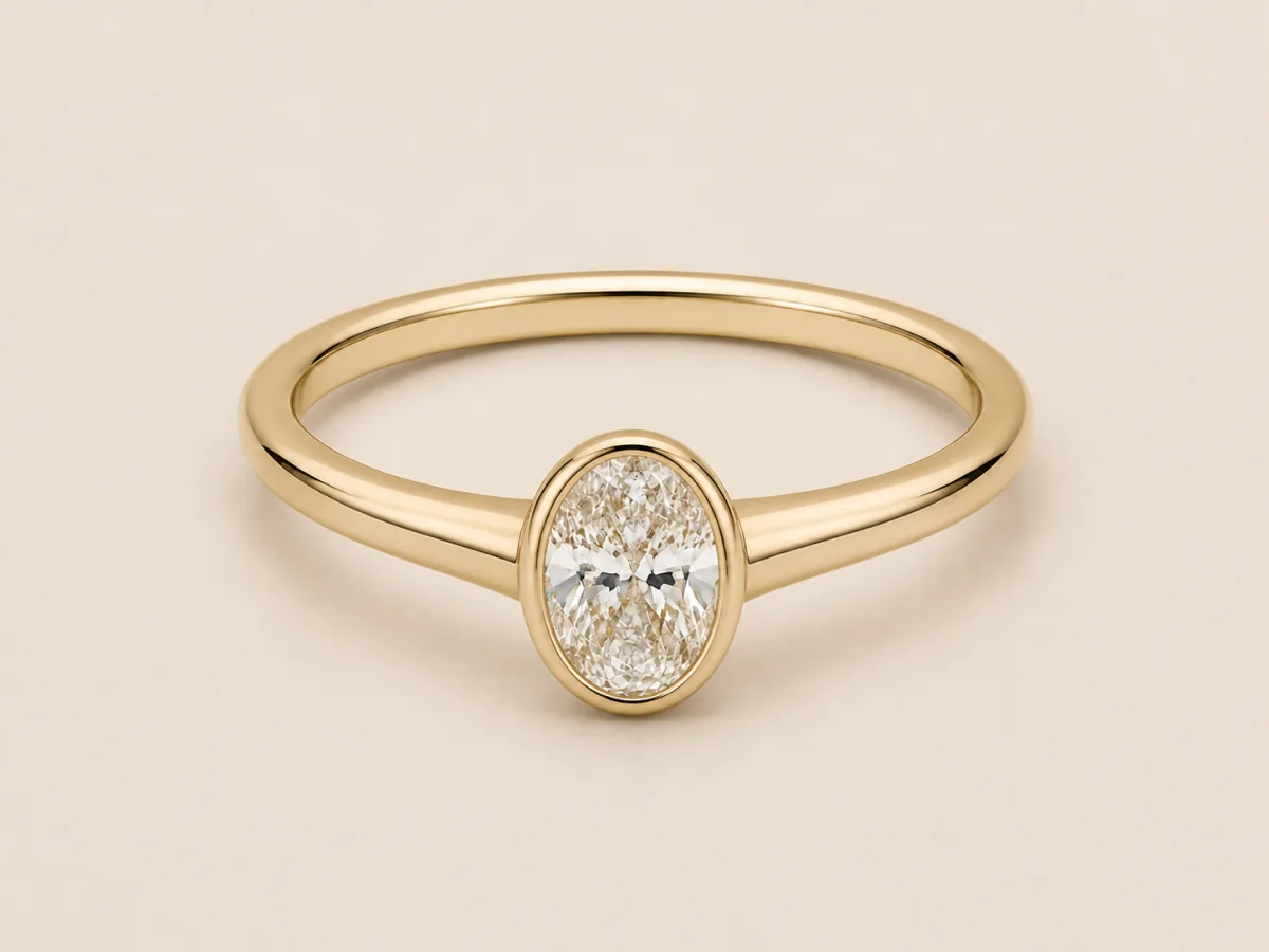 Yellow-gold oval bezel ring with a smooth low setting and connected shoulders, shown in a three-quarter product view.